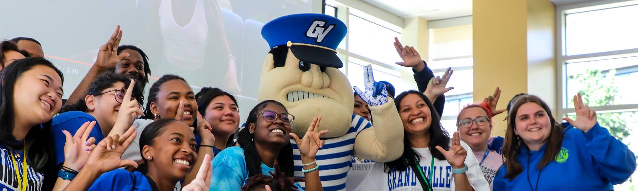 A group of students gather around Louie the Laker as the all make the "Anchors Up" hand symbol.